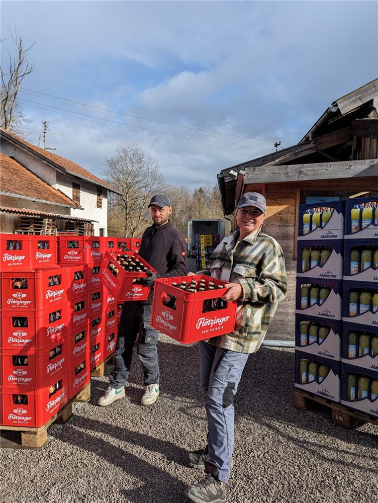Zwei Mitarbeiter tragen Getränkekästen vor dem Markt